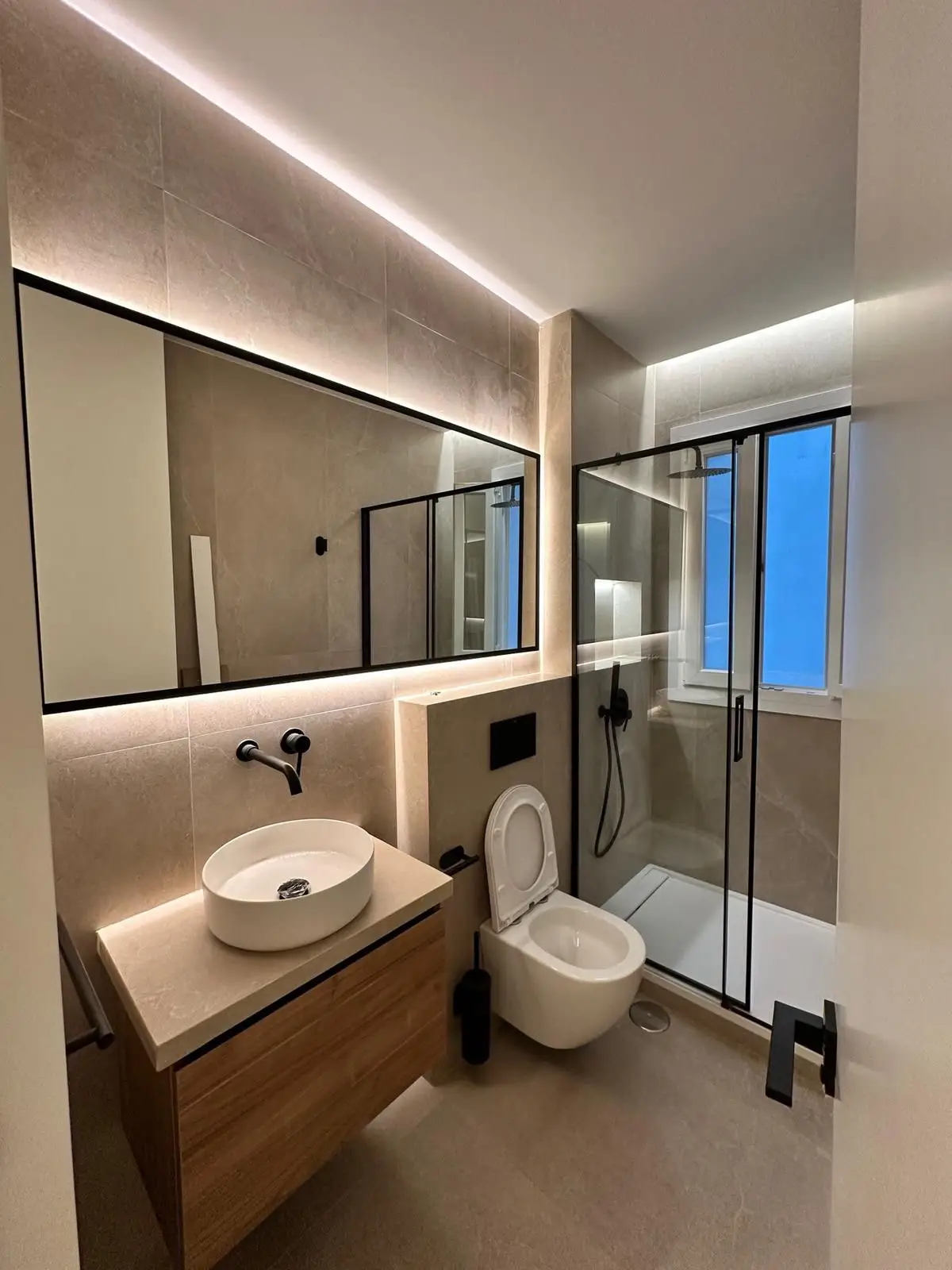 Reforma de baño con iluminación LED indirecta, lavabo sobre encimera y perfilería negra en Madrid