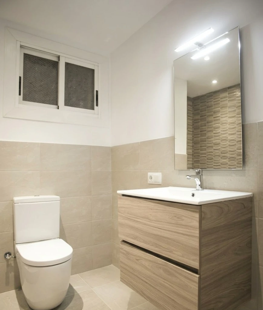 Reforma de baño con mueble de madera suspendido, lavabo blanco y espejo rectangular en Madrid