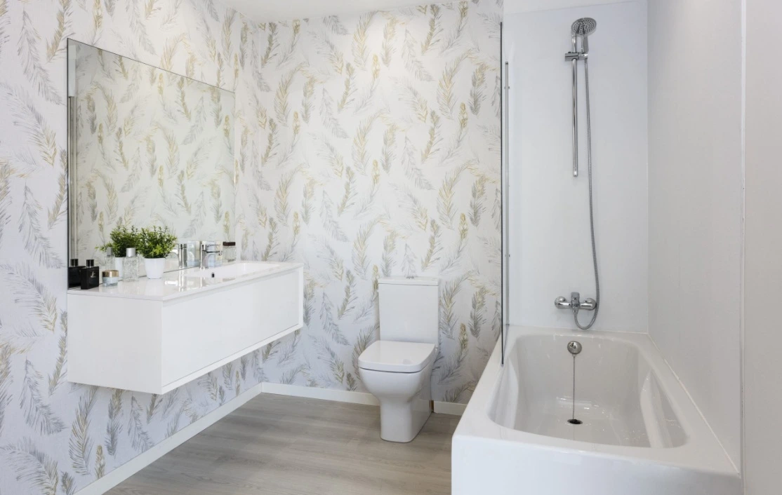 Reforma de baño con papel pintado de motivos vegetales, mueble suspendido blanco y bañera en Madrid