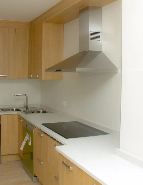 Reforma de cocina con campana extractora de acero, mobiliario de madera clara y encimera blanca en Madrid