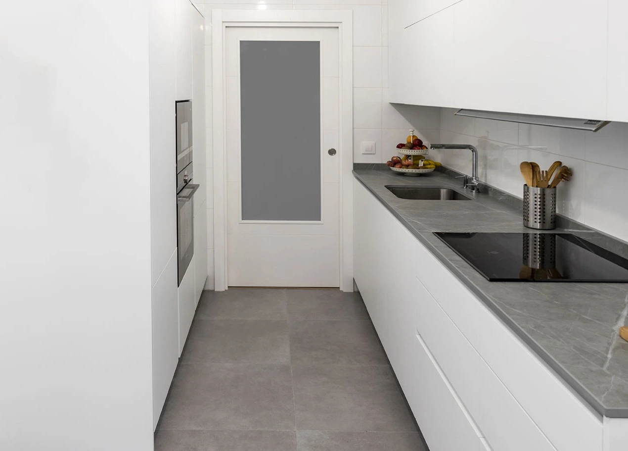 Reforma de cocina con encimera gris efecto piedra, mobiliario blanco minimalista y suelo cerámico en Madrid