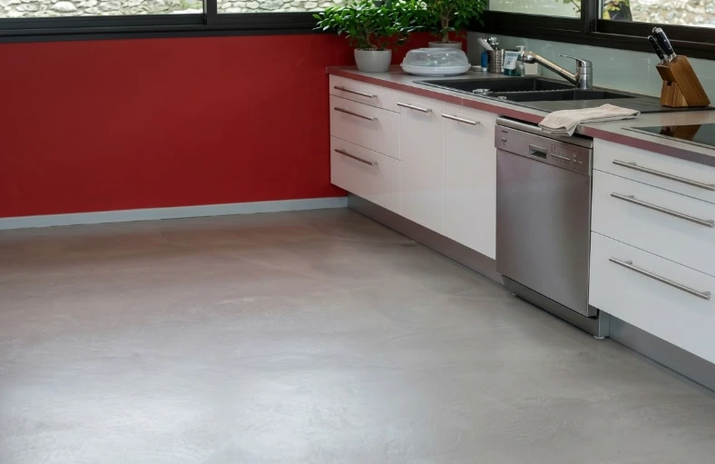 Reforma cocina con suelo de microcemento gris, mobiliario blanco y pared de contraste roja en Madrid