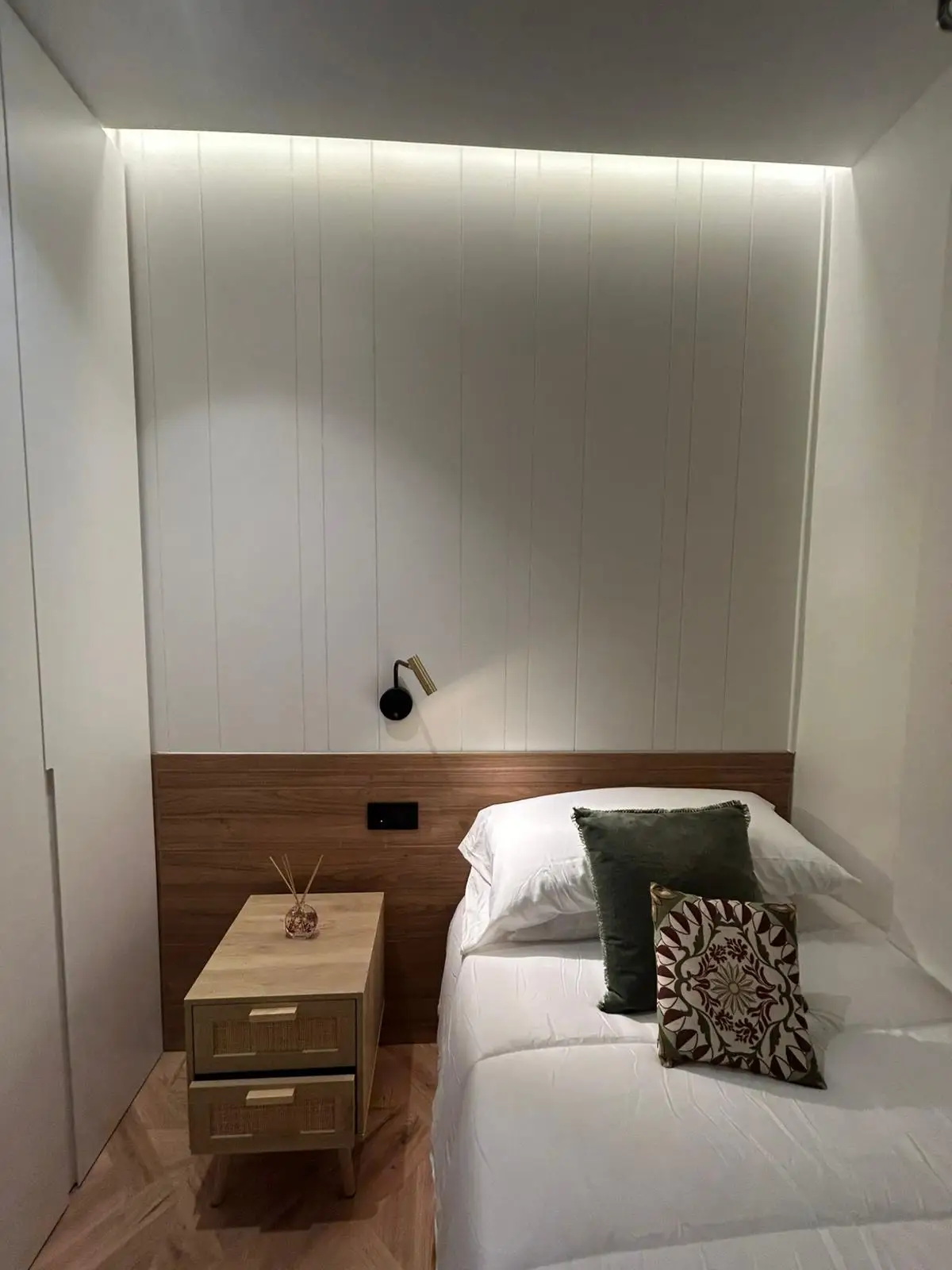 Reforma vivienda con cabecero de madera, iluminación LED foseada y panelado blanco en Madrid